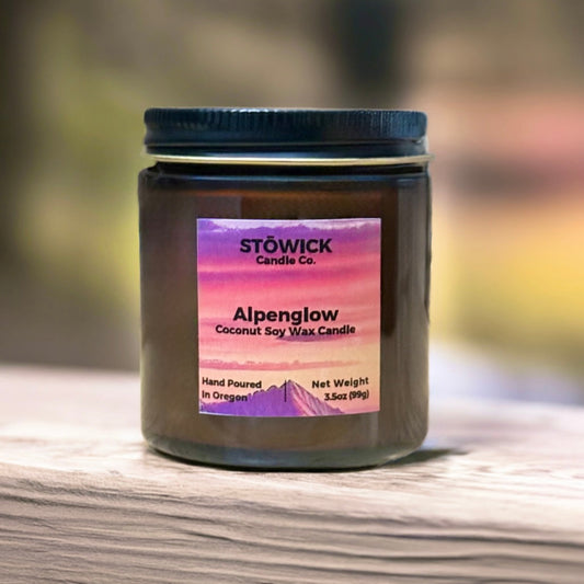 a mini 3.5oz candle in an amber jar sitting outside on a rail with an alpenglow fragrance