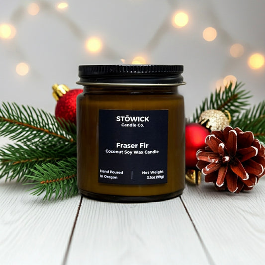 A scented Fraser fir mini candle in a glass amber jar on a white table.