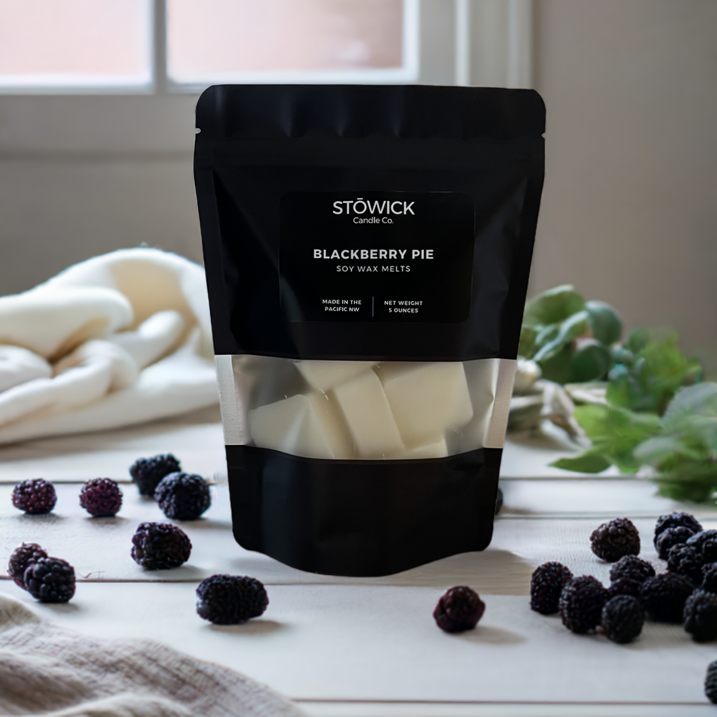 a 5 ounce black bag of pure soy wax blackberry pie melts sitting on a table next to blackberries