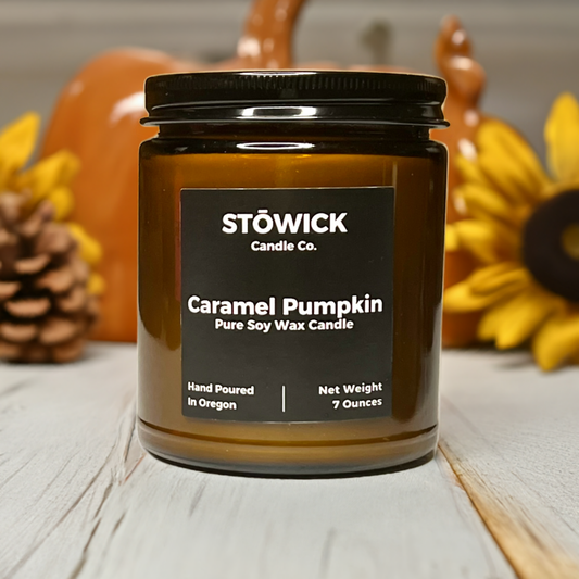 a caramel pumpkin jar candle in an amber jar sitting on a white table with fall decor. The candle is 7oz and has a black lid.