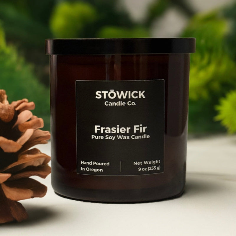 Stowick Candle Co. Frasier Fir tumbler candle with a pine cone on a blurred green background