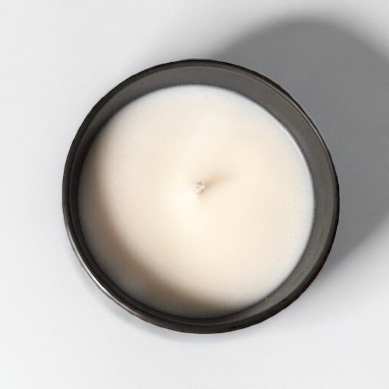 A birds eye view of a huckleberry scented candle by Stowick candles. The candle is in a black jar with white wax.