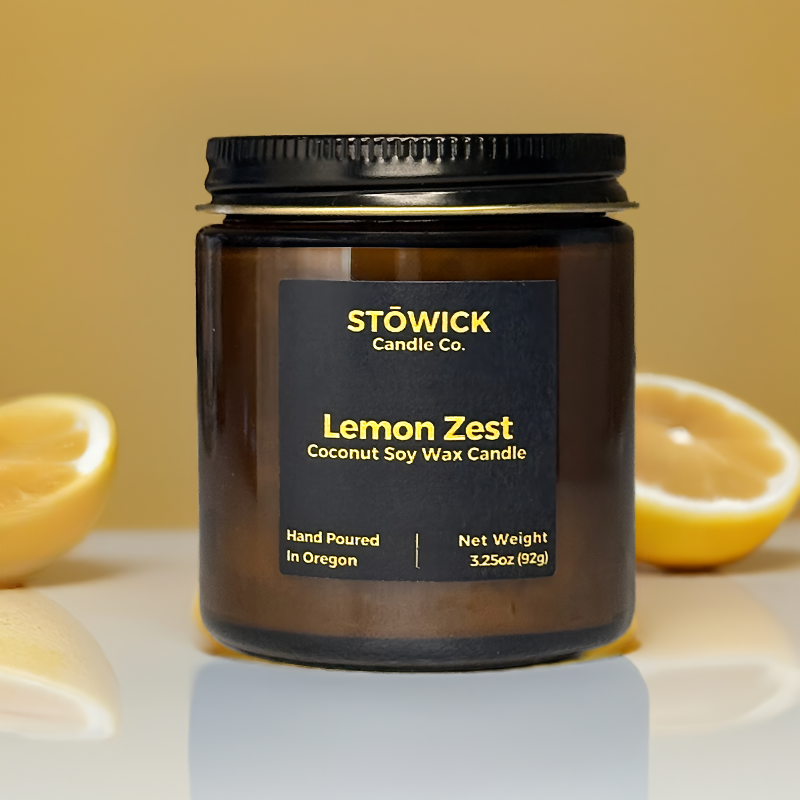 lemon zest mini soy coconut wax candle in an amber jar sitting on a table with lemons behind it