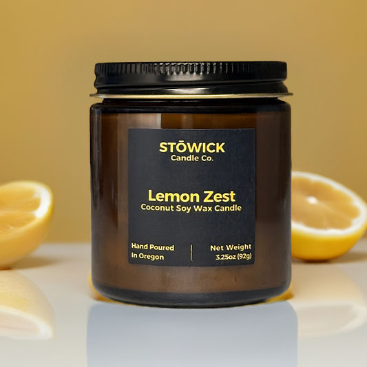 lemon zest mini soy coconut wax candle in an amber jar sitting on a table with lemons behind it