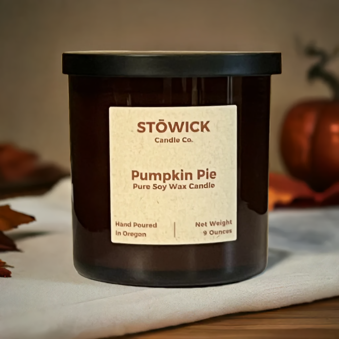 A pumpkin pie scented pure soy wax candle in a 9 ounce jar with a black lid sitting on top of a wood table by fall decor