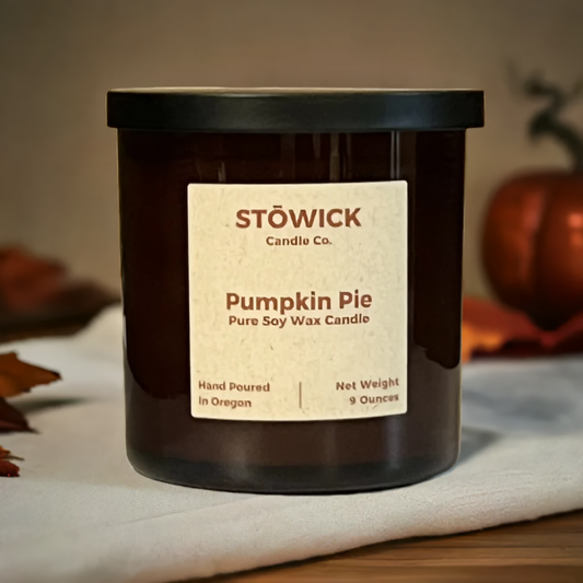 A pumpkin pie scented pure soy wax candle in a 9 ounce jar with a black lid sitting on top of a wood table by fall decor