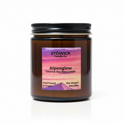 Alpenglow mini candle in an amber jar with a brightly colored pink label 