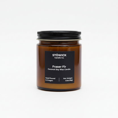 A fraser fir mini candle in an amber jar with an all white background. 