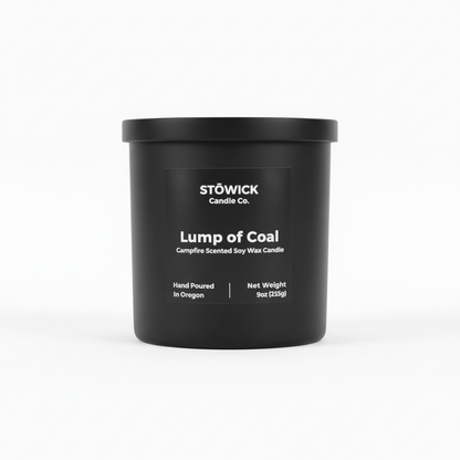 A lump of coal scented tumbler candle in a black jar with a black label and white background 