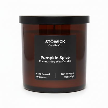 A pumpkin spice tumbler candle in an amber jar with a black label and an all white background 