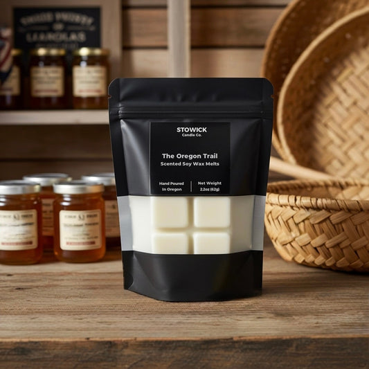 The Oregon trail wax melts in black packaging on a wooden surface with jars and a basket in the background