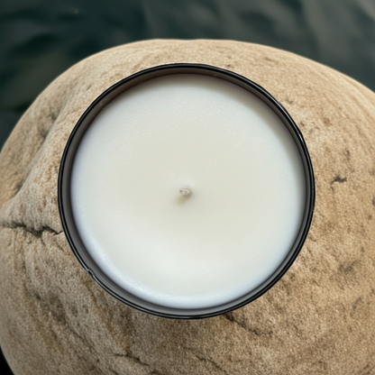 Candle in a black jar on a rock with water in the background with the Oregon trail fragrance