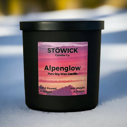 a soy wax candle with the fragrance alpenglow in a black jar sitting in the snow