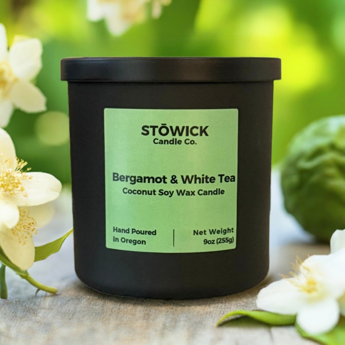 A bergamot and white tea candle sitting outside surrounded by jasmine flowers. The candle is in a black jar with a green label 