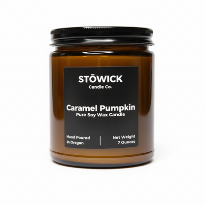 A caramel pumpkin scented candle in an amber jar with a black lid against a white background 