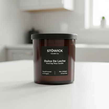 dulce de leche tumbler candle with a black label in an amber jar on a white surface