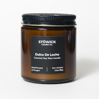 A dulce de leche mini candle in an amber jar with a white background and black label 