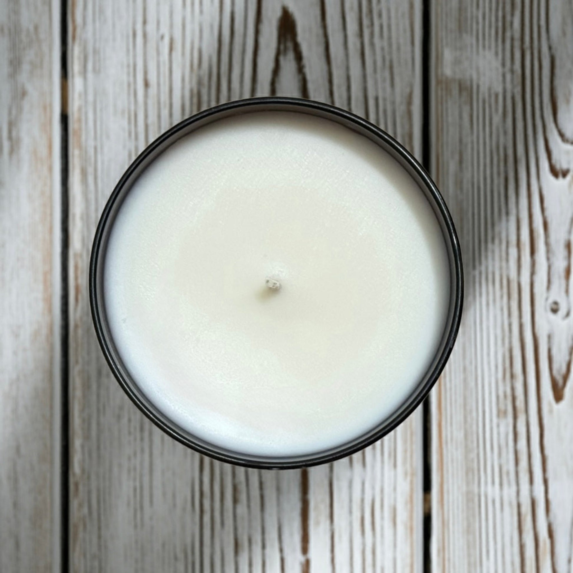 White fall and santal candle in a black container on a wooden surface