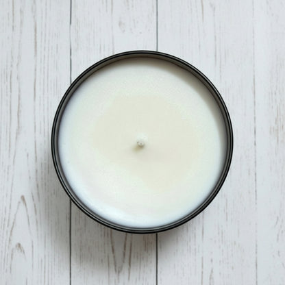 White fall and santal candle in a black container on a wooden surface
