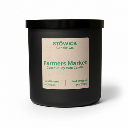 A farmers market fragranced tumbler candle in a black jar with a brown label and white background 