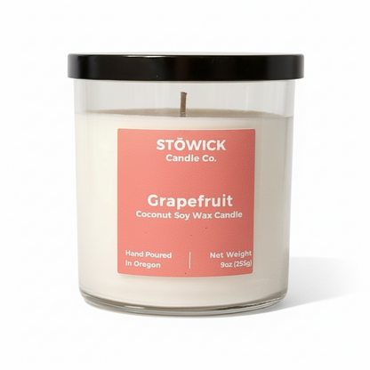 A grapefruit scented tumbler candle in a glass jar with a peach colored label