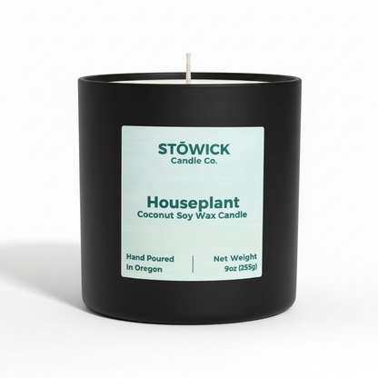 A house plant scented tumbler candle in a black jar with the lid off on a white background