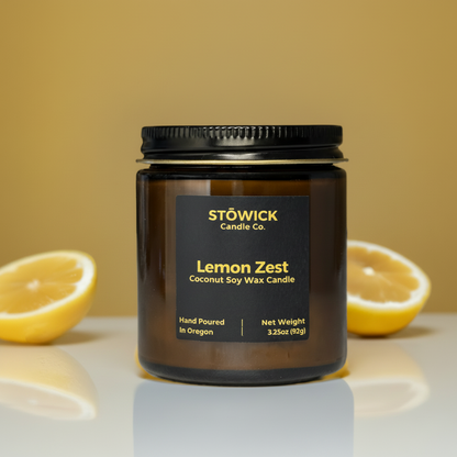 lemon zest mini soy coconut wax candle in an amber jar sitting on a table with lemons behind it