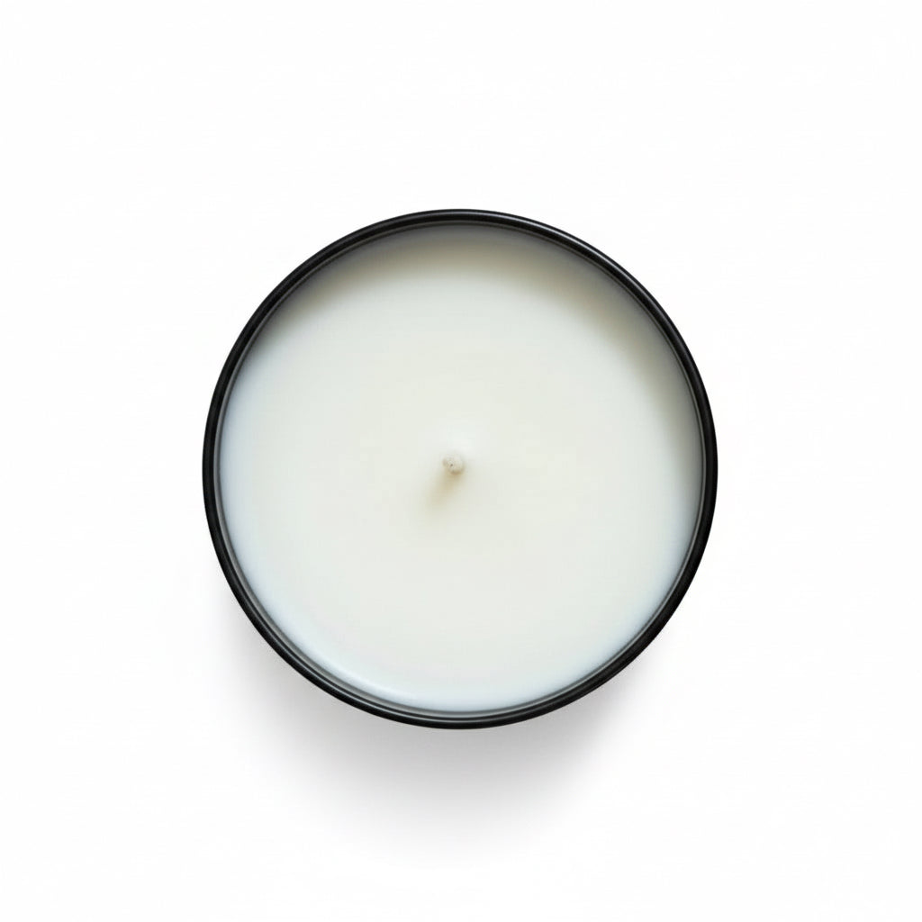 White candle in a black container on a white surface 