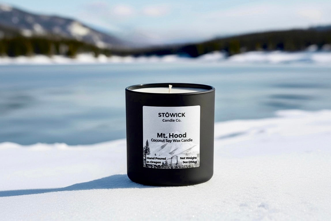Black candle with a label on a snowy surface with a mountain and lake in the background
