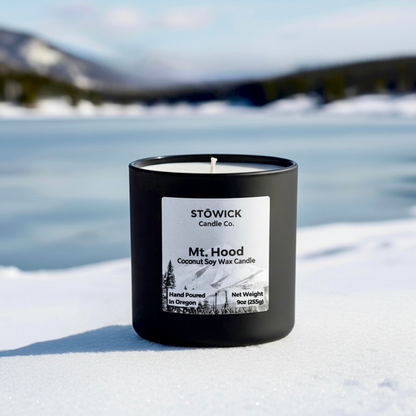 A mt hood tumbler candle in a black jar against a snowy alpine background 
