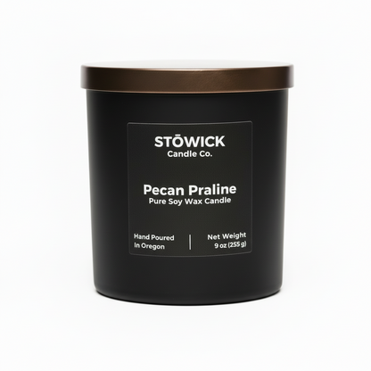 A pecan praline tumbler candle in a black jar with a bronze lid and white background 