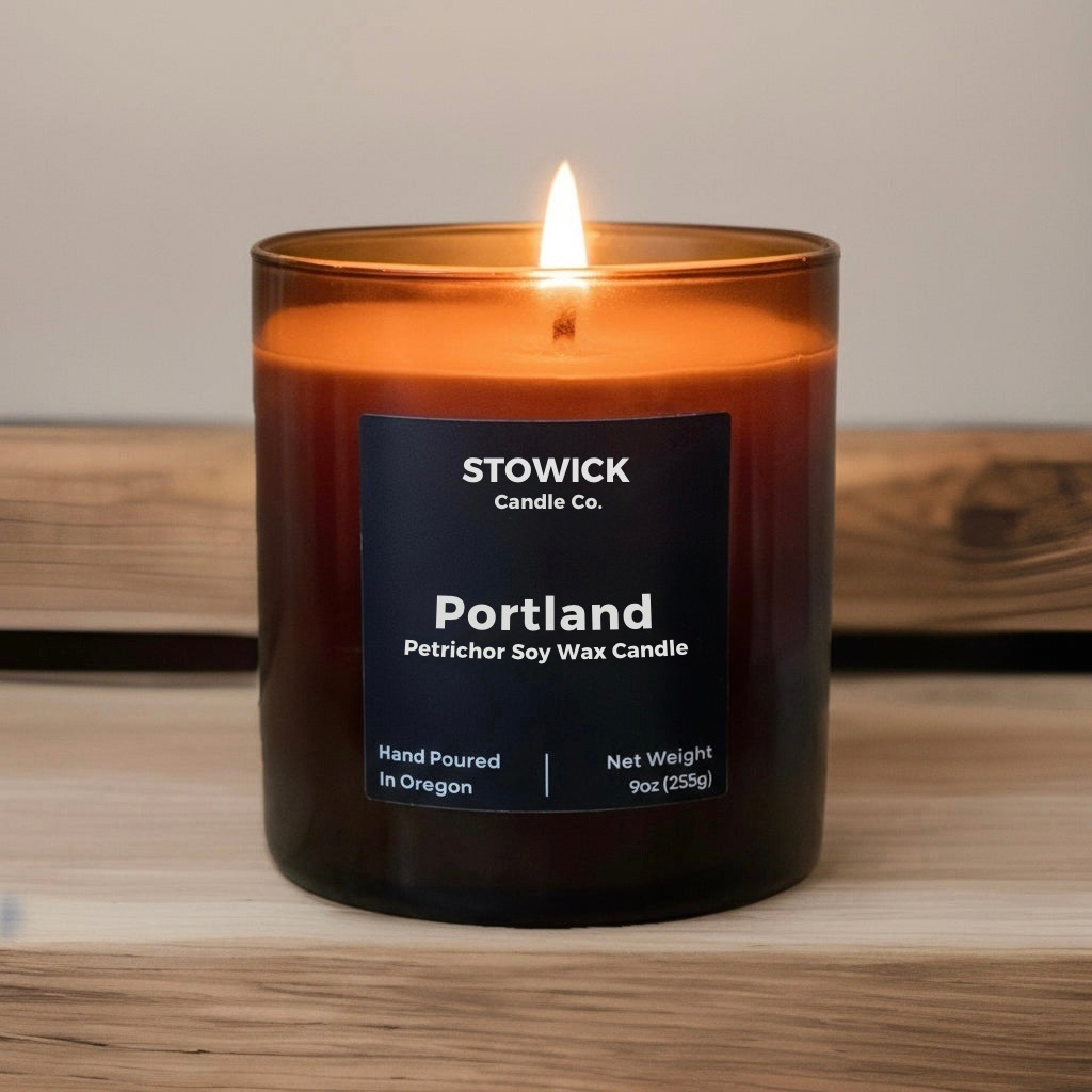 A Portland tumbler candle in an amber jar in a wood table with a black lid 