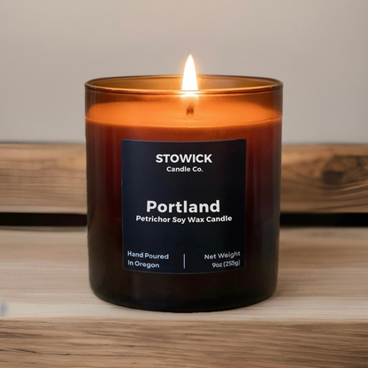 A Portland tumbler candle in an amber jar in a wood table with a black lid 