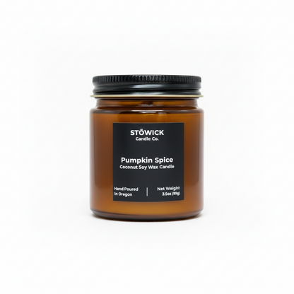 A pumpkin spice mini candle in an amber jar with a black label against a white background 