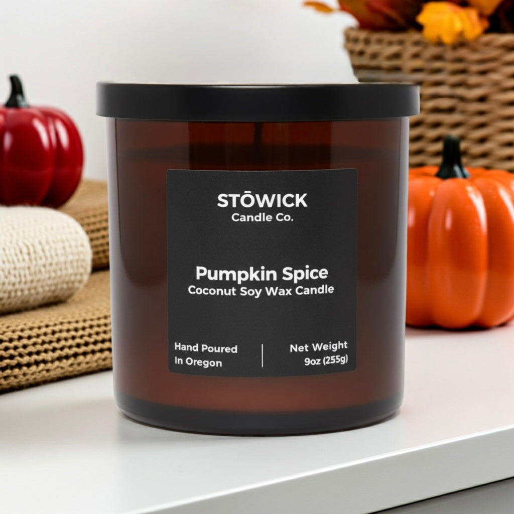 A pumpkin spice tumbler candle in an amber jar on a white wood table near fall decor